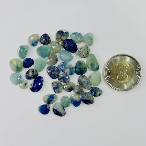 Assorted blue and green gemstones with a coin for scale on a white background