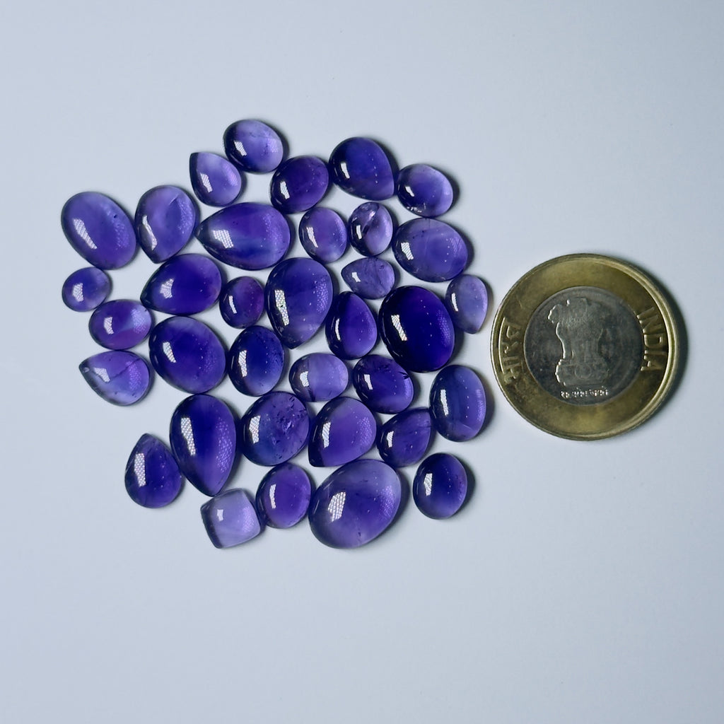 Purple teardrop-shaped stones with a coin for scale on a White background