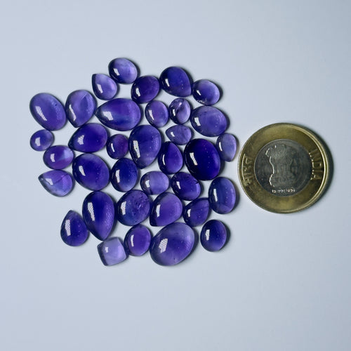 Purple teardrop-shaped stones with a coin for scale on a White background