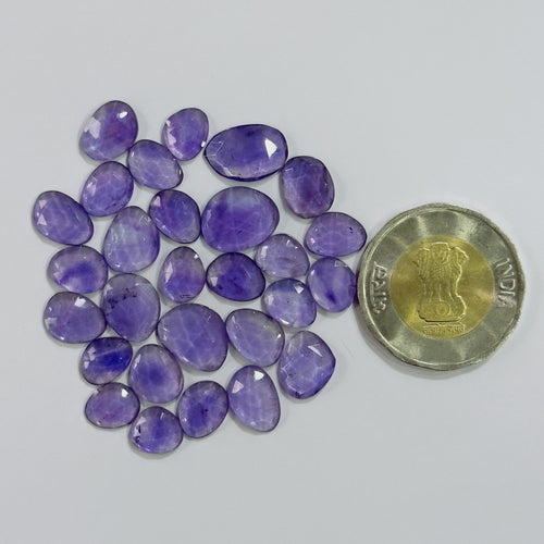 Purple gemstones with a coin for scale on a light gray background