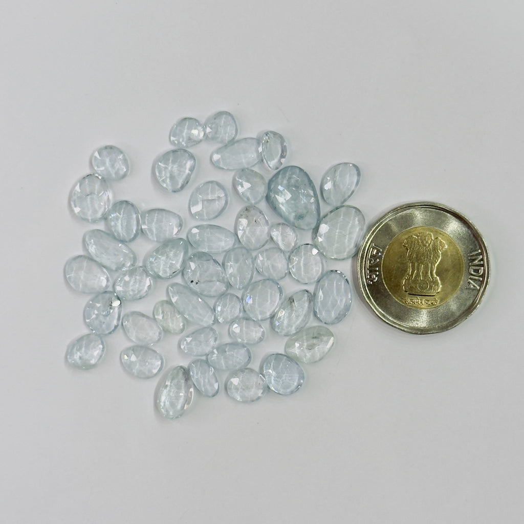 Collection of light blue gemstones next to a coin on a white background