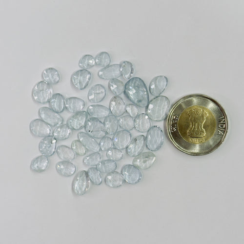 Collection of light blue gemstones next to a coin on a white background