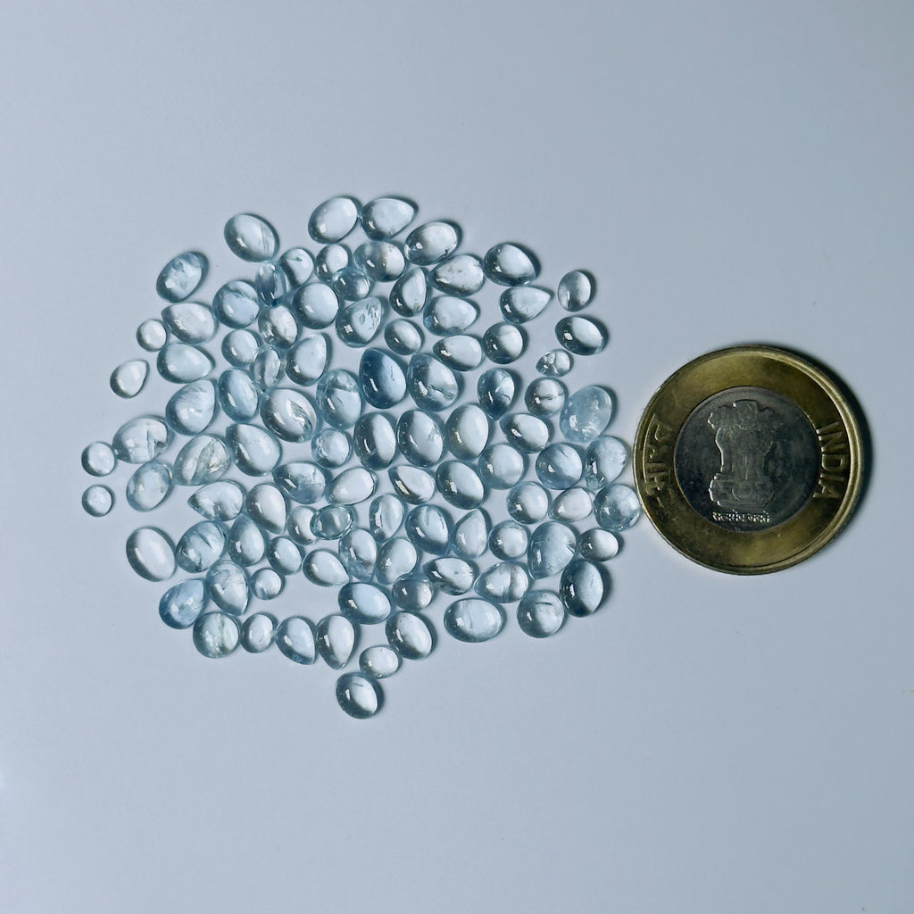 Clear Blue glass pebbles next to a coin on a light gray background