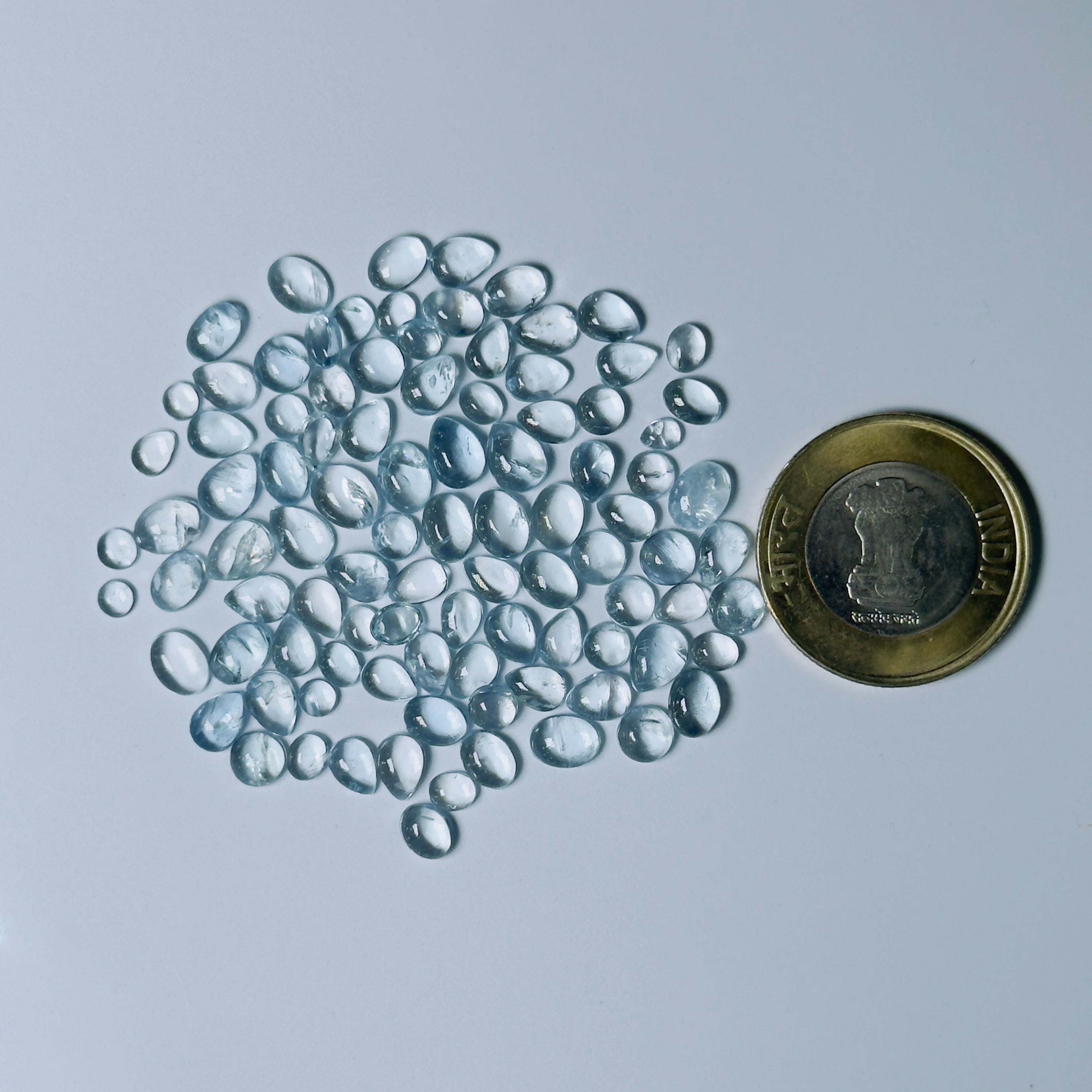 Clear Blue glass pebbles next to a coin on a light gray background