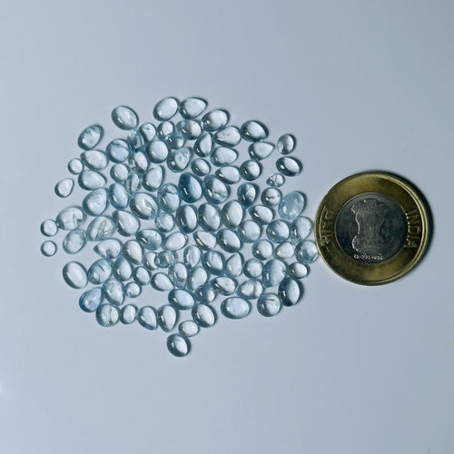 Clear Blue glass pebbles next to a coin on a light gray background