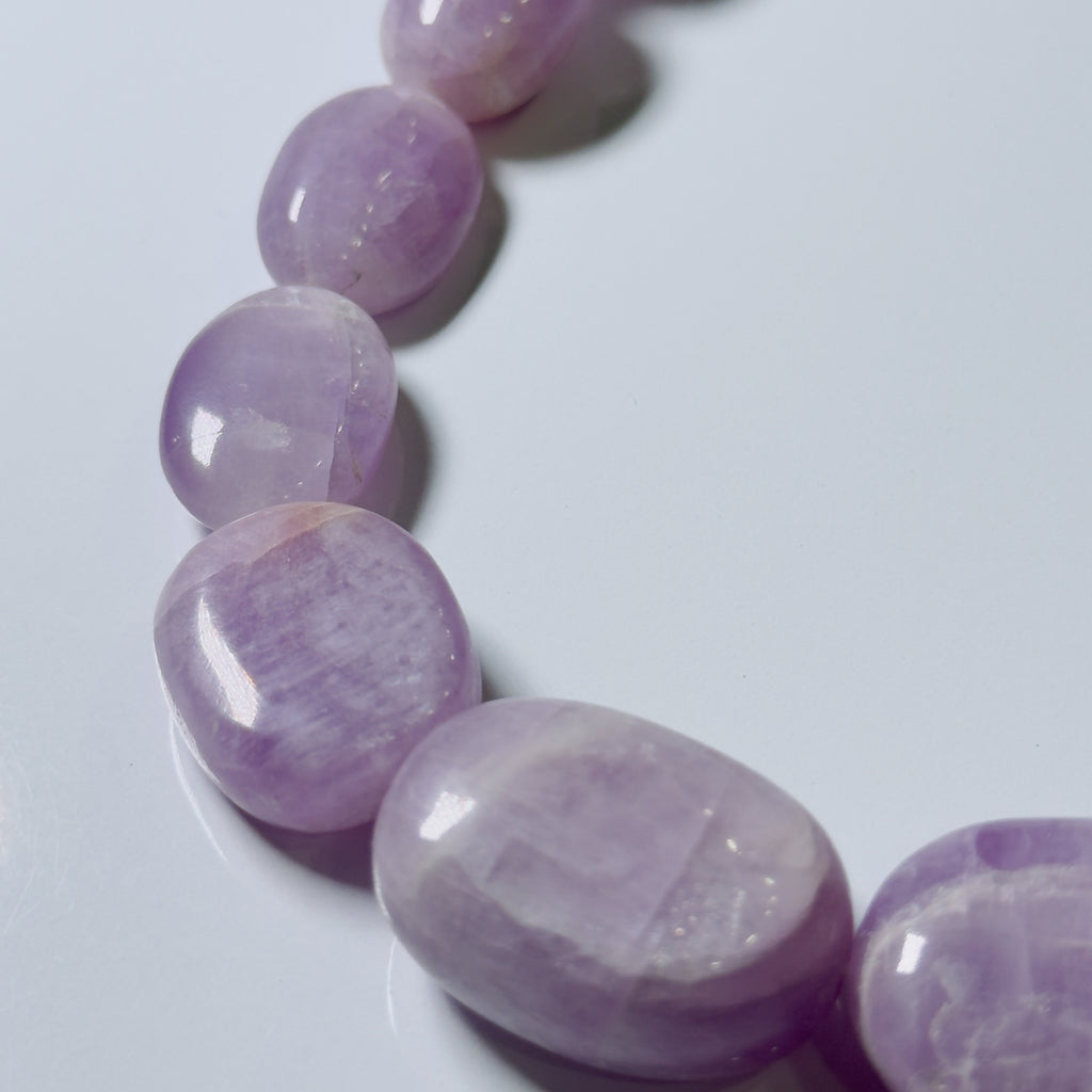 A close-up of a polished purple gemstone bead strand, likely amethyst, on a light gray background.
