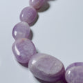 A close-up of a polished purple gemstone bead strand, likely amethyst, on a light gray background.