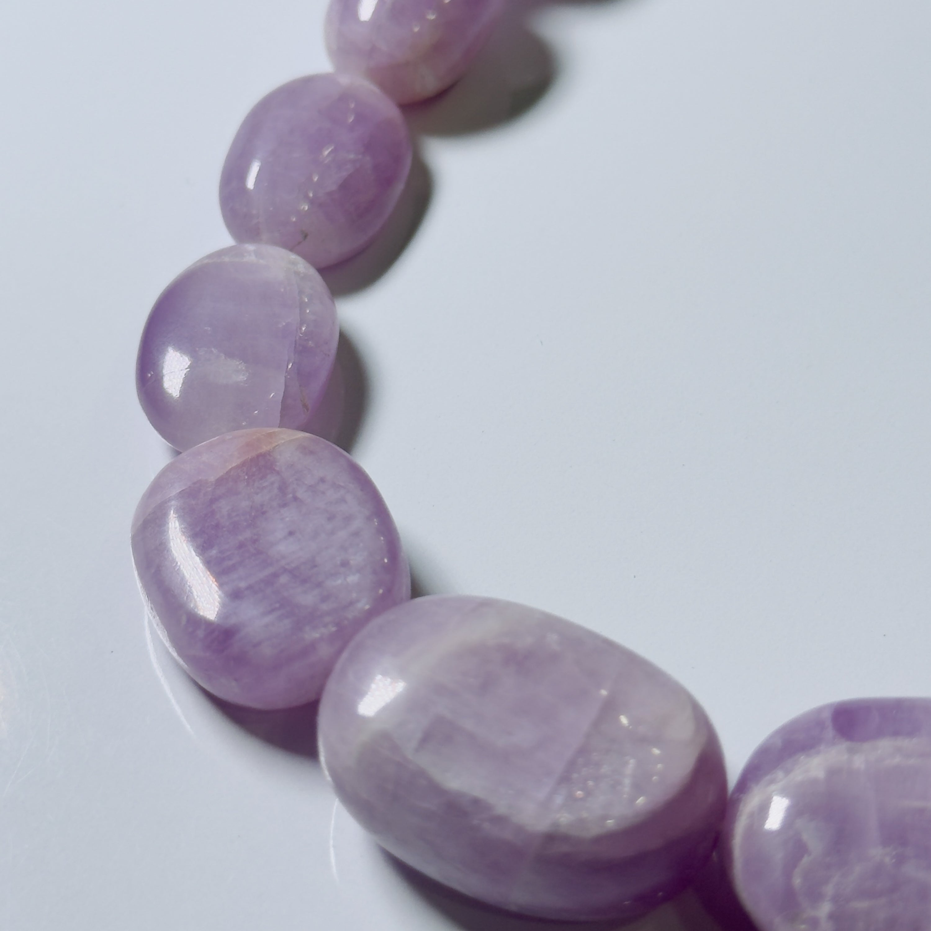 A close-up of a polished purple gemstone bead strand, likely amethyst, on a light gray background.