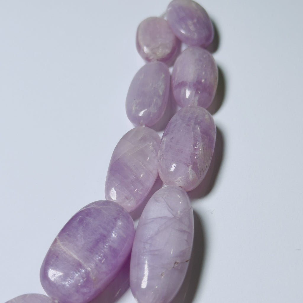 A strand of polished purple amethyst gemstone beads or pendants arranged diagonally on a plain white background.