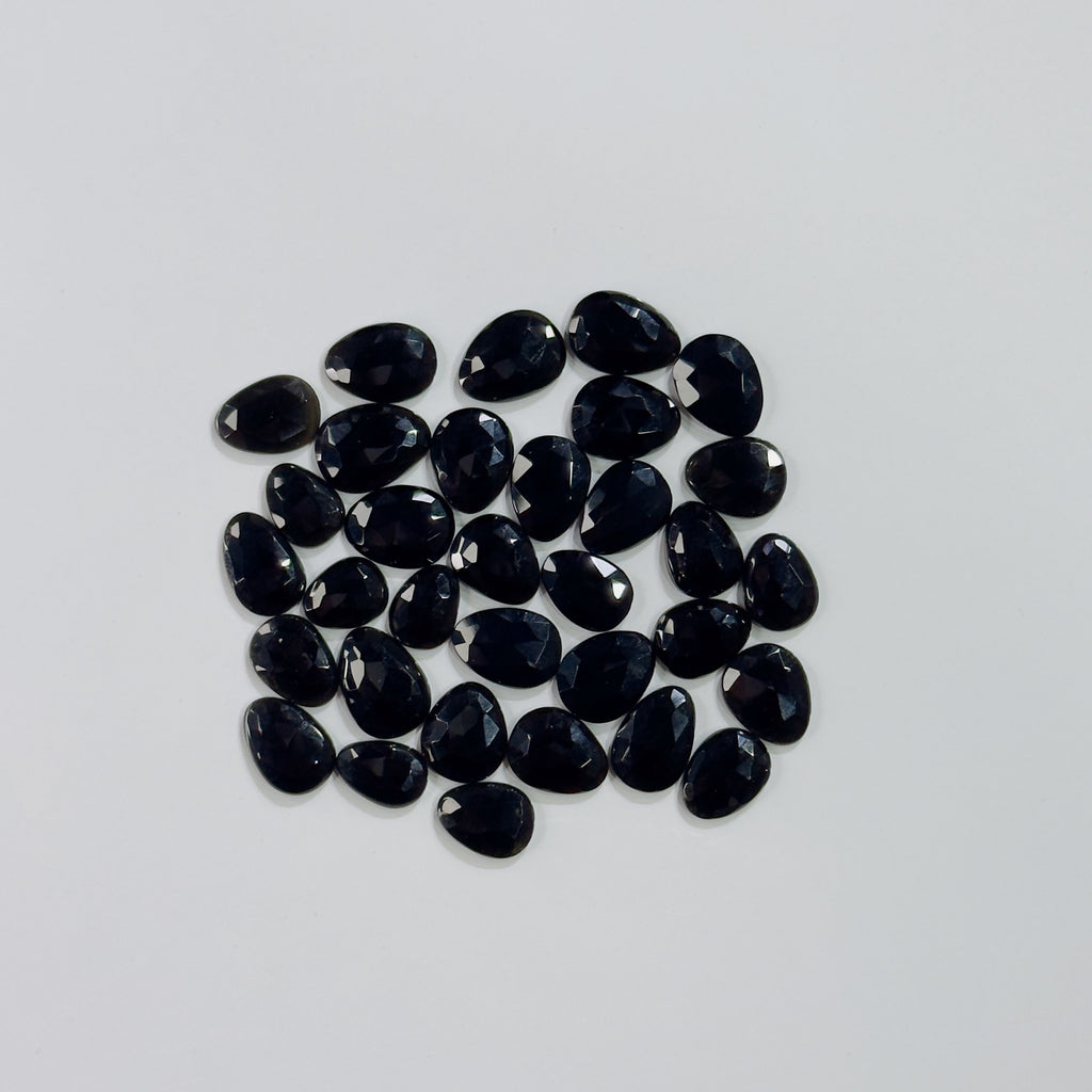 Collection of black teardrop-shaped gemstones on a light gray background