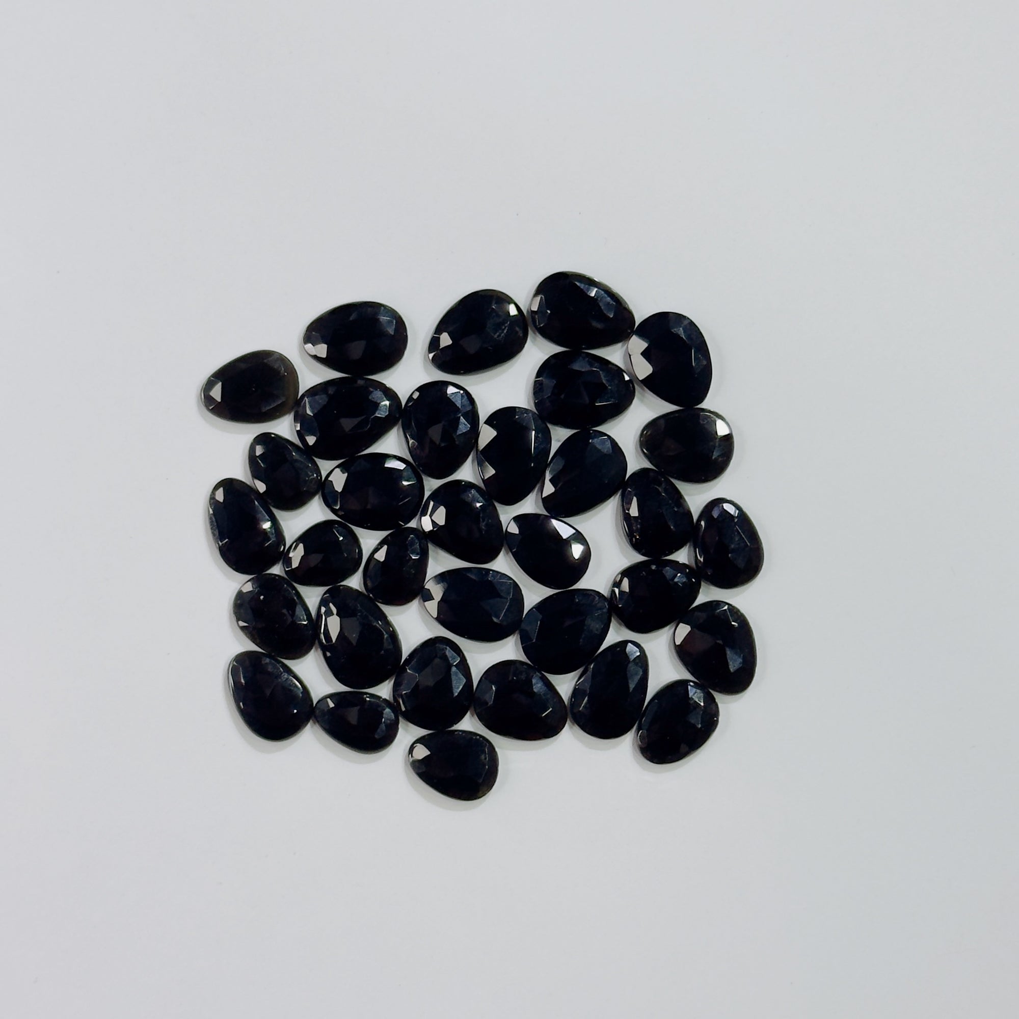 Collection of black teardrop-shaped gemstones on a light gray background