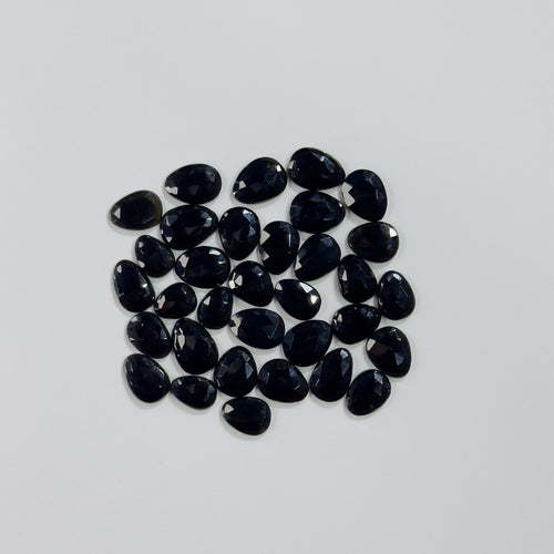 Collection of black teardrop-shaped gemstones on a light gray background