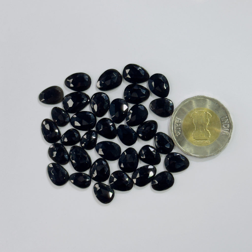 Black gemstones with a coin for scale on a white background