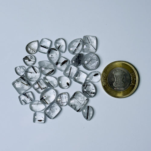 Collection of rough diamonds with a coin for scale on a White background