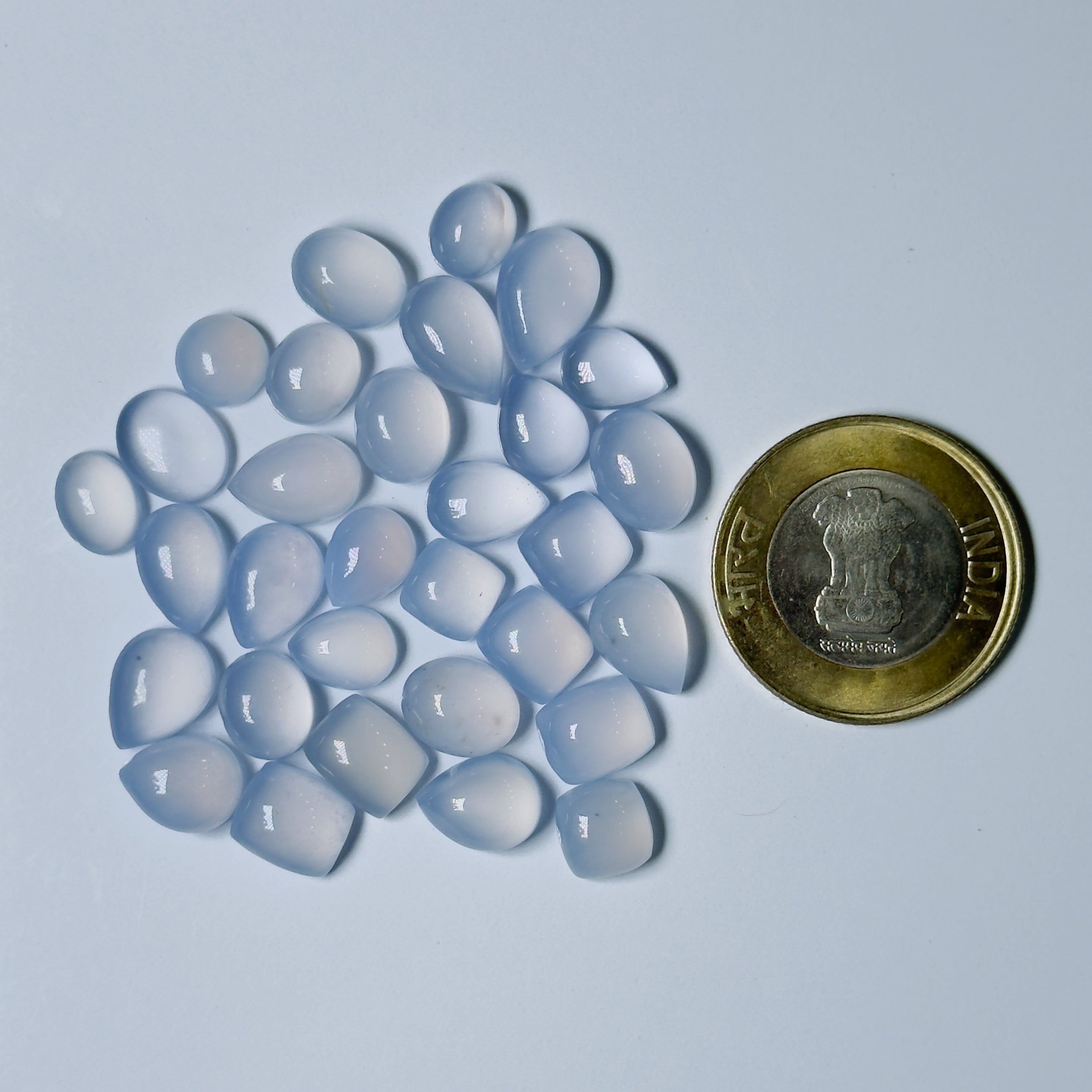 Blue chalcedony stones with a coin for scale on a light blue background