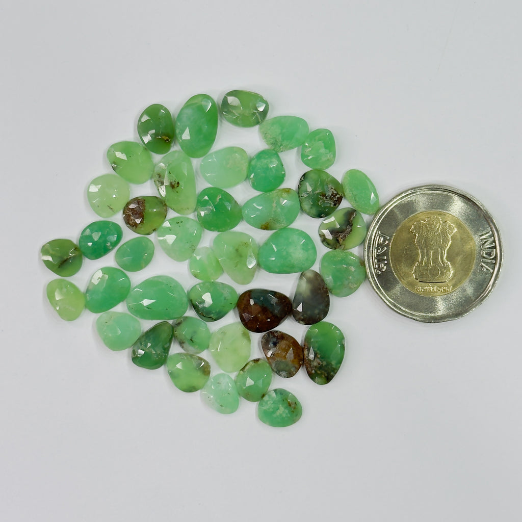 Green gemstones with a coin for scale on a white background