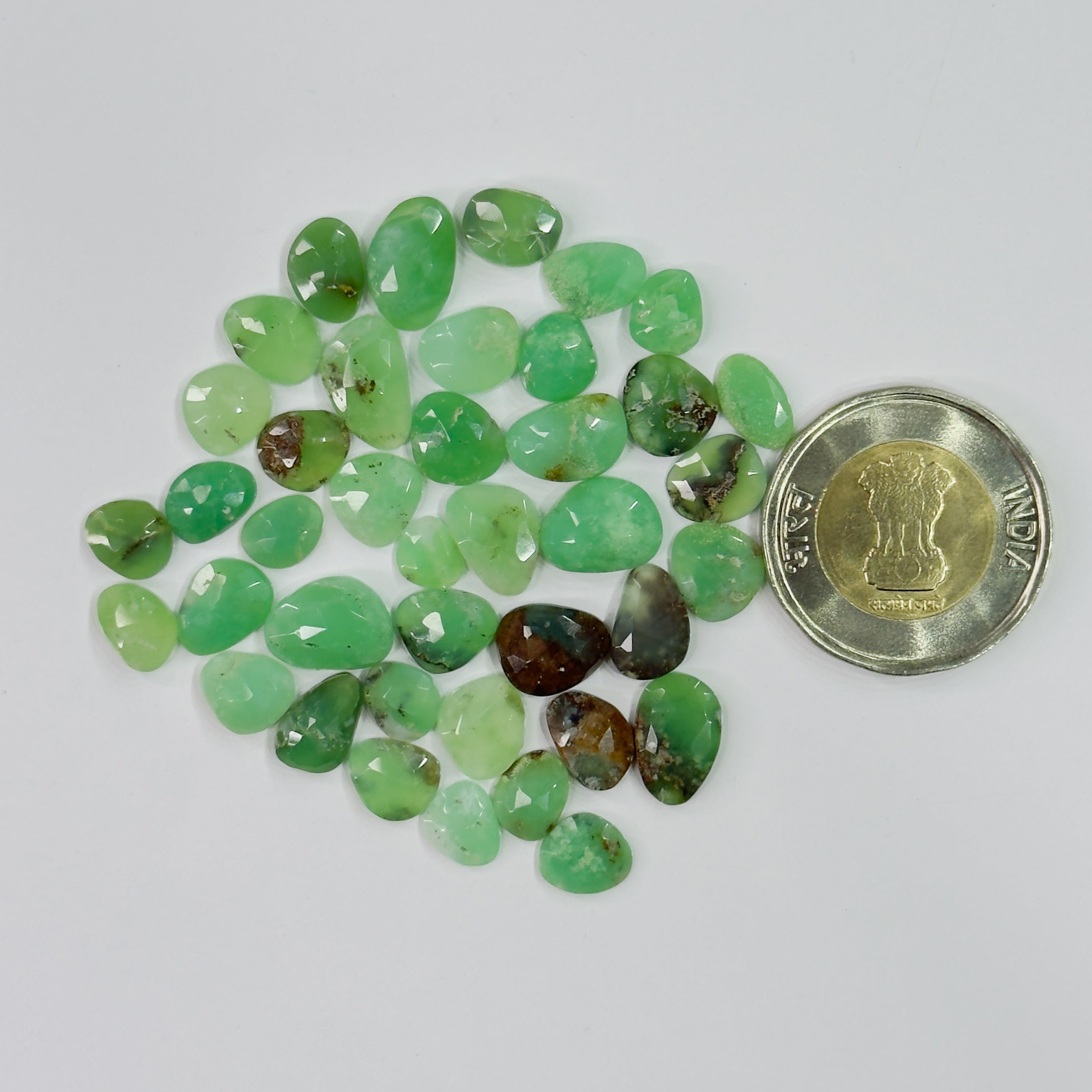 Green gemstones with a coin for scale on a white background
