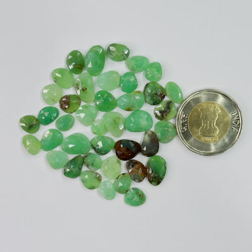 Green gemstones with a coin for scale on a white background