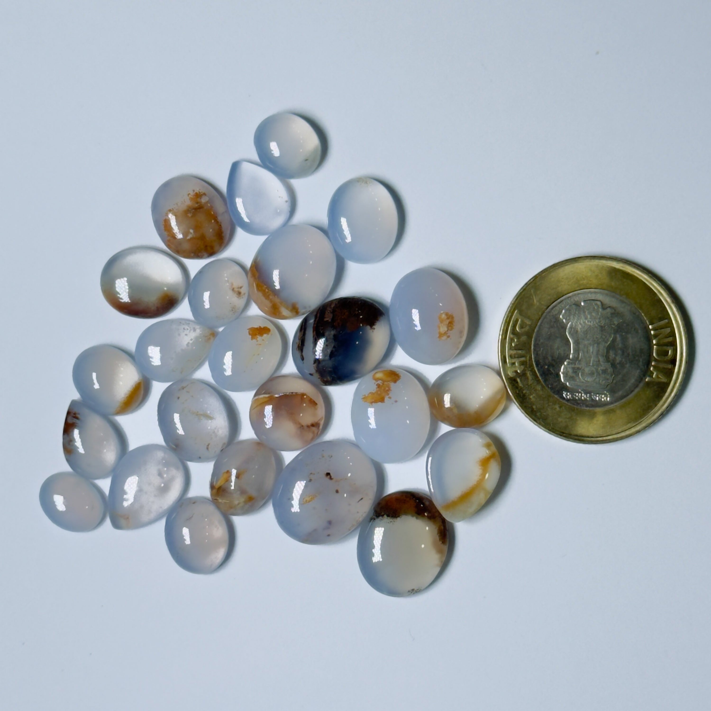 Collection of teardrop-shaped agate stones with a coin for scale on a white