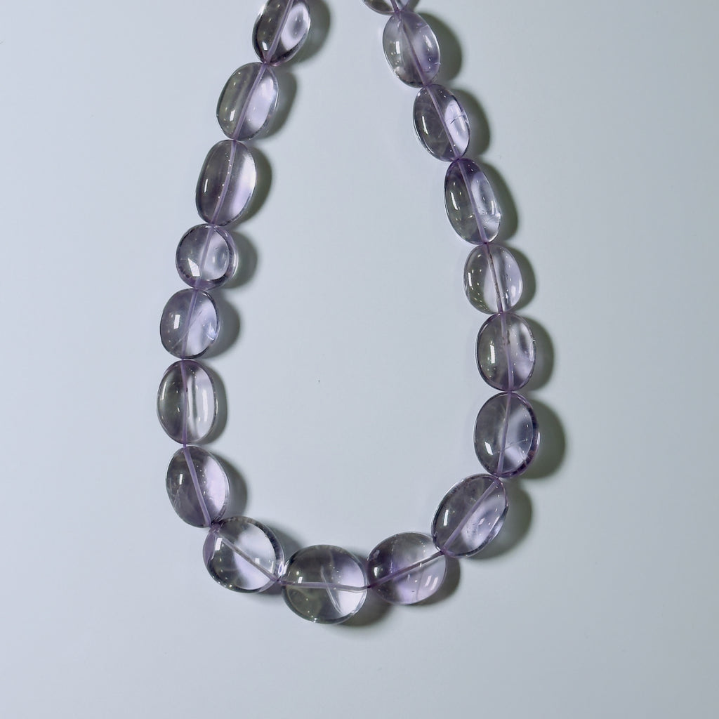 A beaded necklace made of smooth, oval-shaped translucent purple glass beads, arranged in a U-shape on a light gray background.
