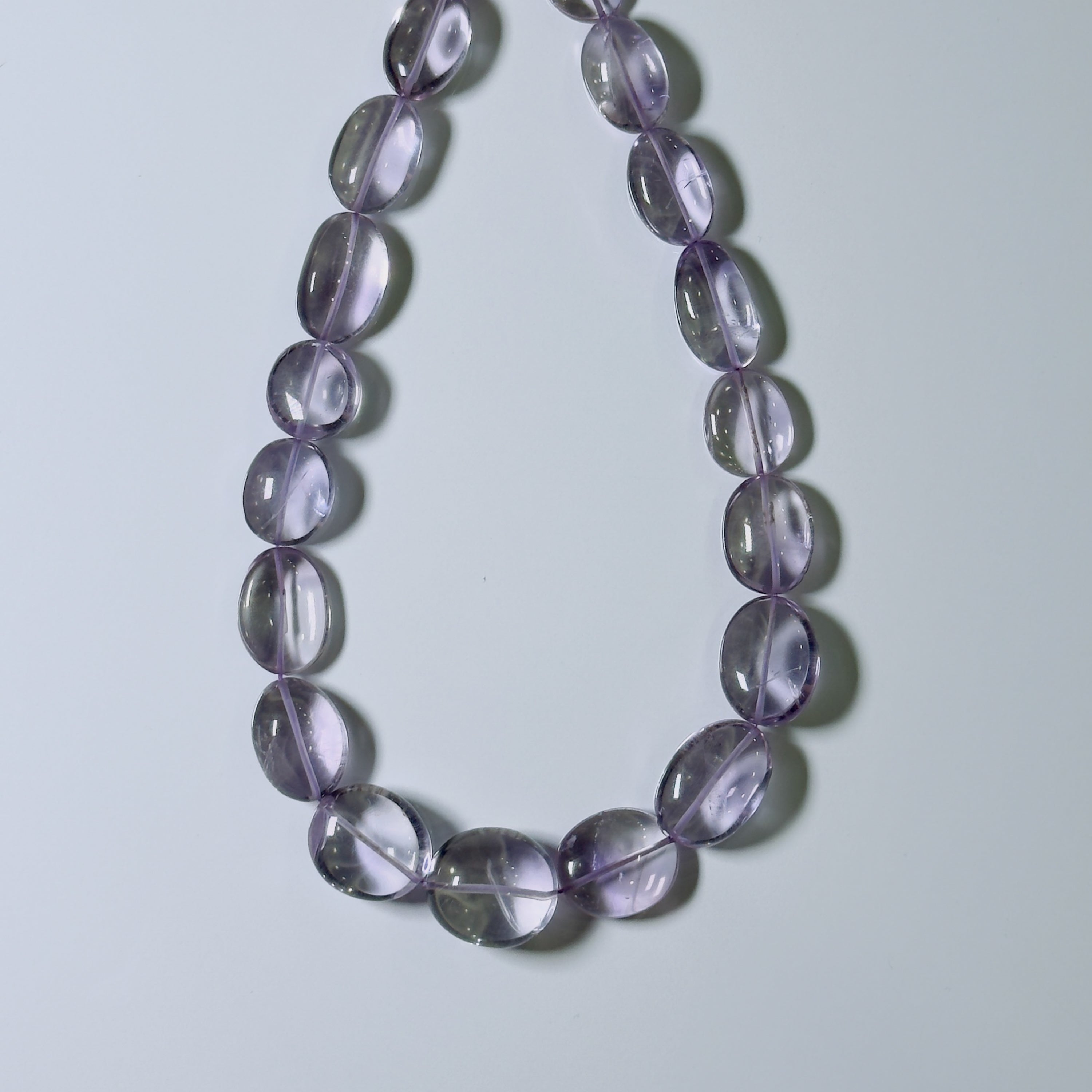 A beaded necklace made of smooth, oval-shaped translucent purple glass beads, arranged in a U-shape on a light gray background.