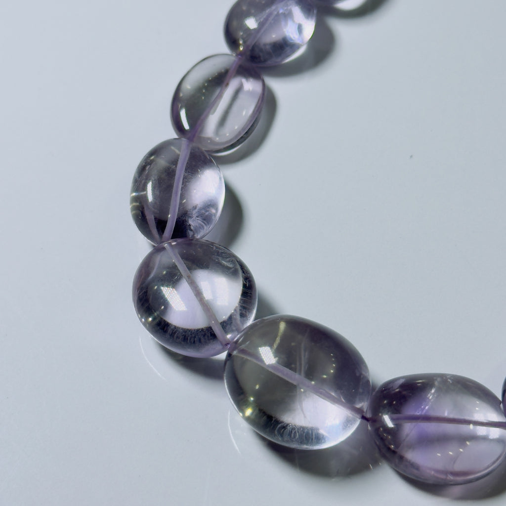 A close-up of a beaded strand with oval translucent purple gemstone beads on a light gray background.