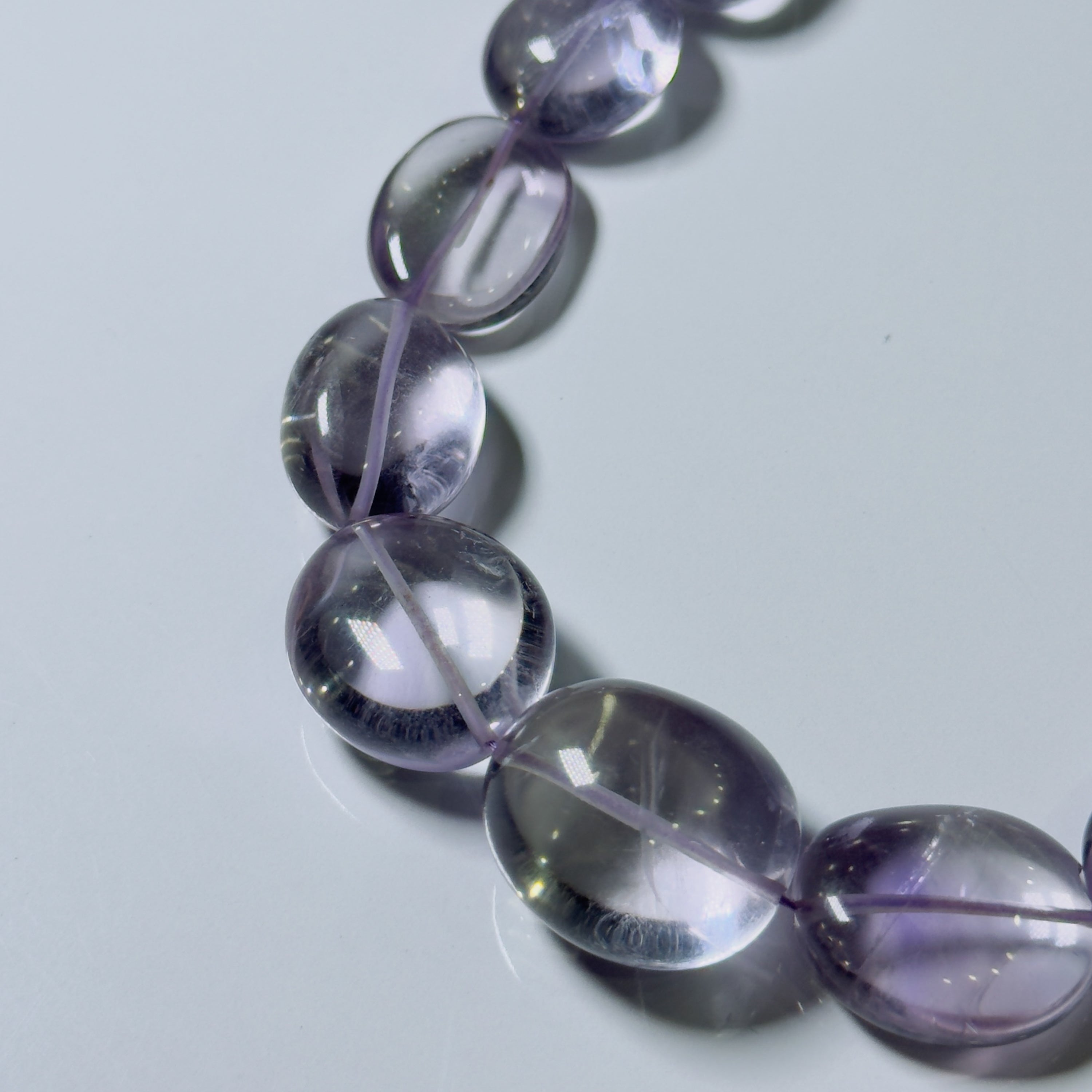 A close-up of a beaded strand with oval translucent purple gemstone beads on a light gray background.