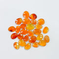 A group of polished, faceted cabochon gemstones in shades of orange, yellow, and red, arranged in a loose pile on a plain white background.