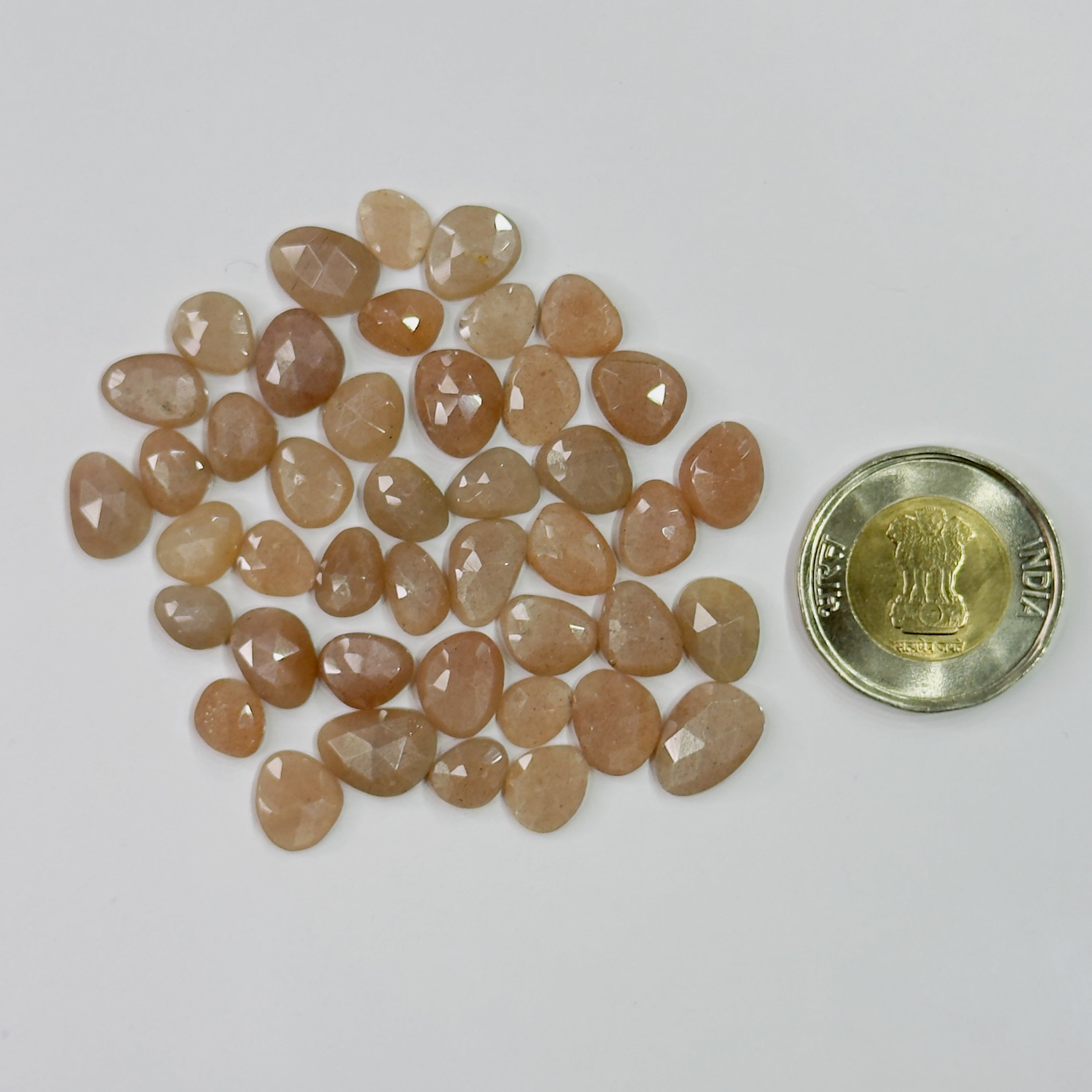 Pile of peach-colored stones next to a coin on a white background