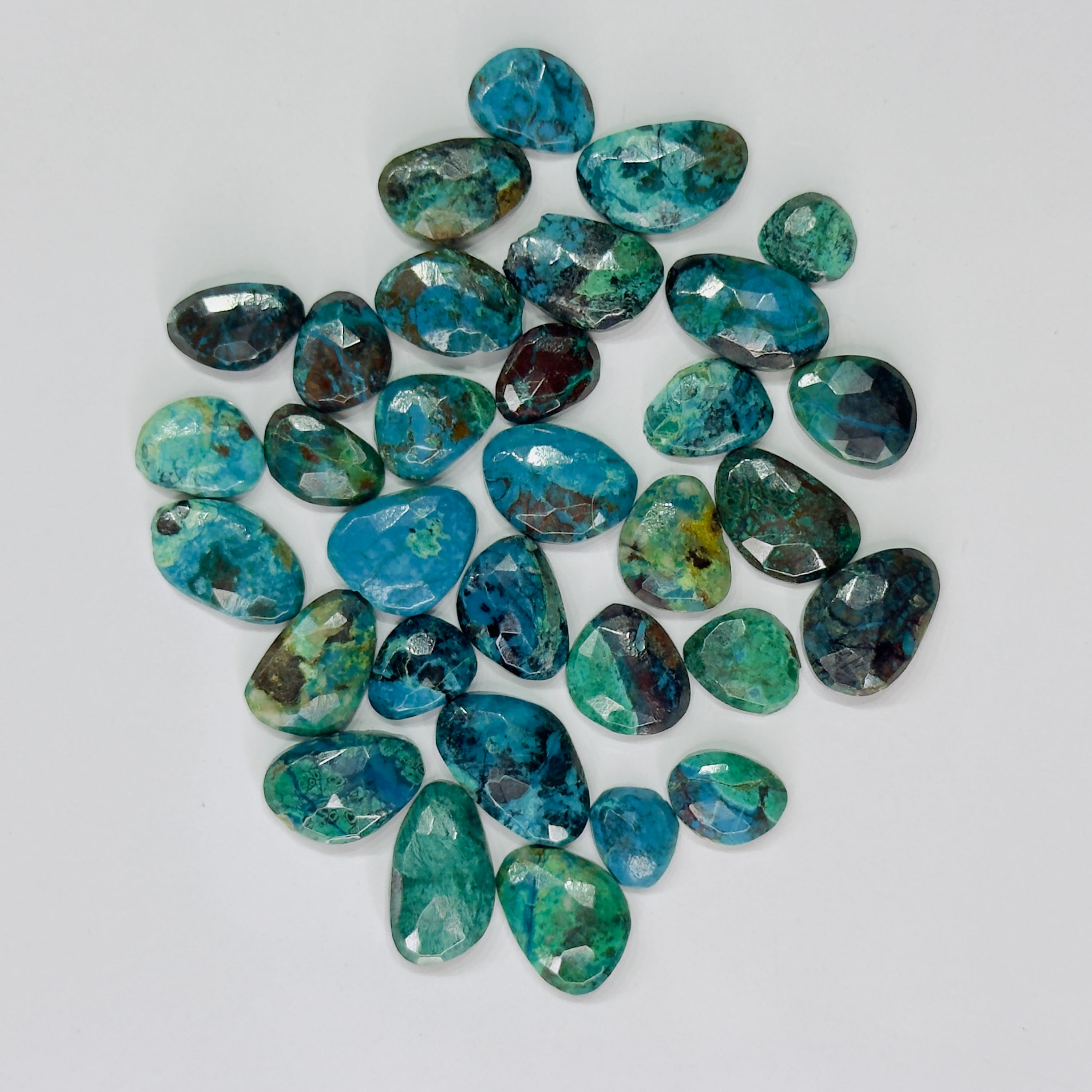 A group of polished tumbled gemstones in shades of turquoise, teal, blue, and green with natural matrix patterns, arranged on a plain white background.