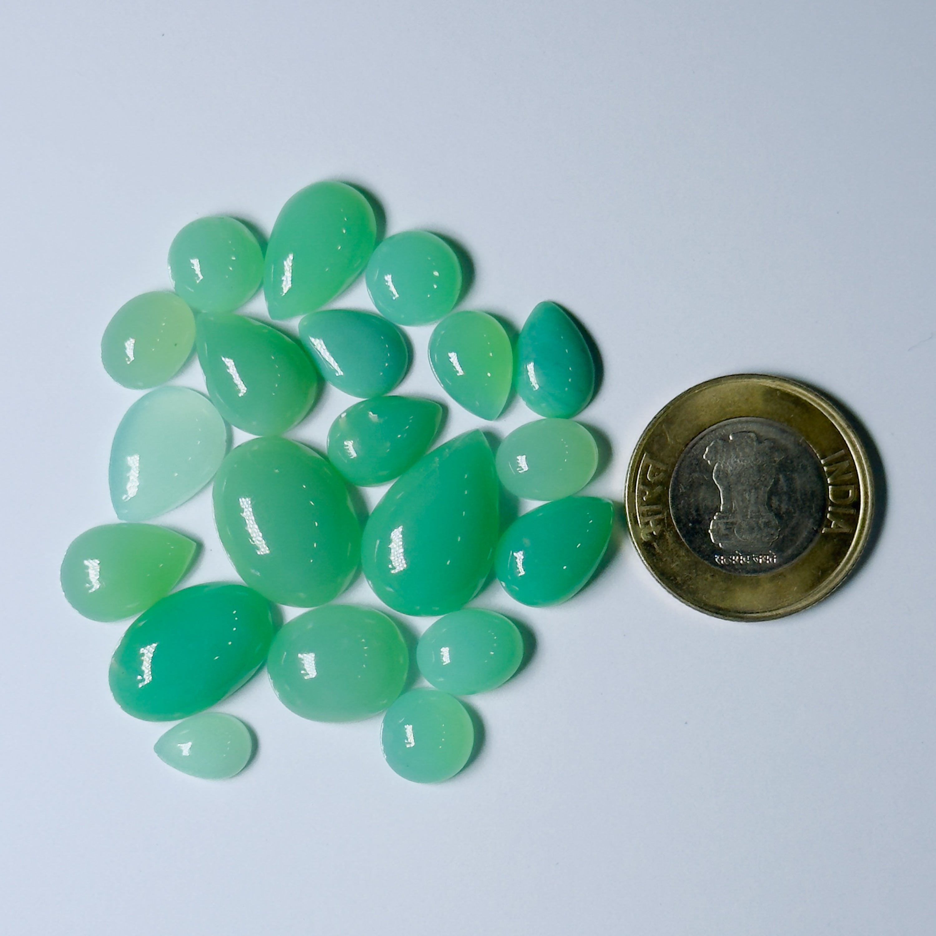 Green teardrop-shaped stones with a coin for scale on a light blue background