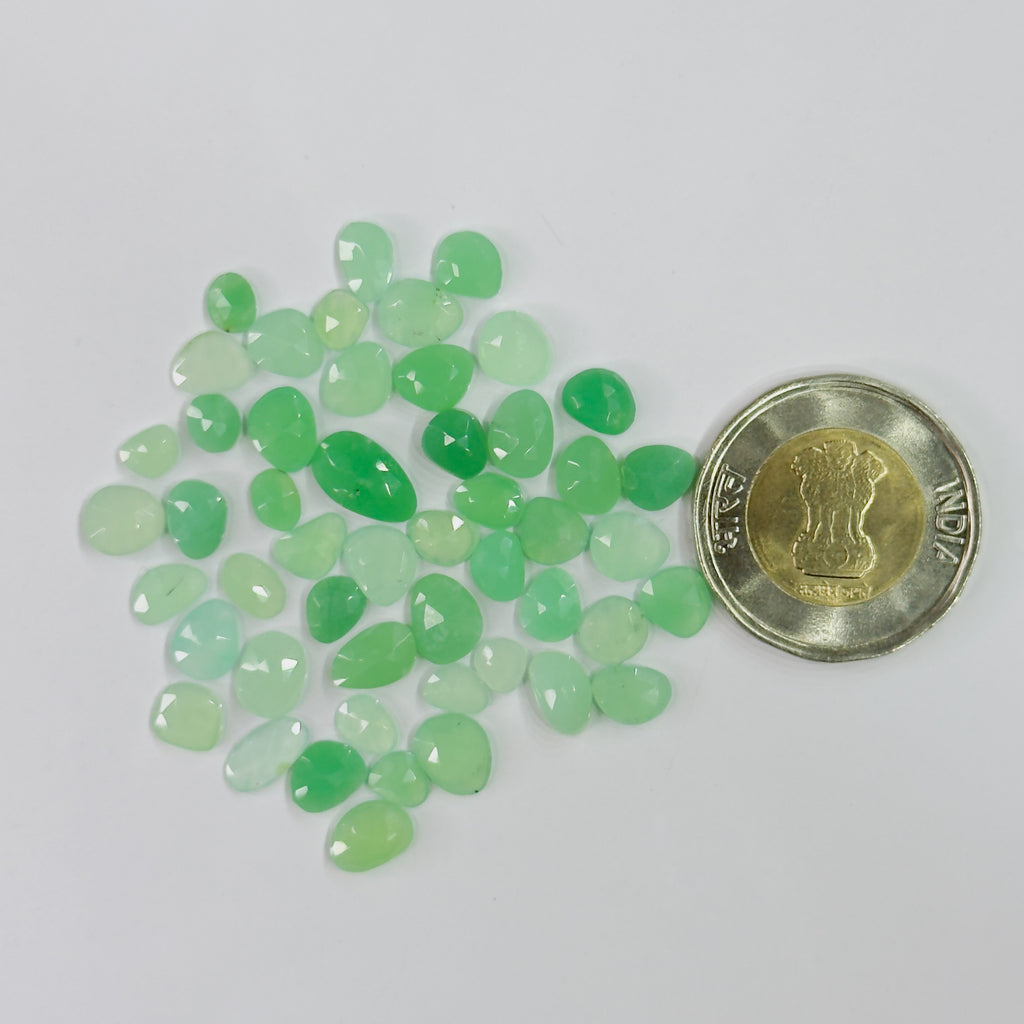 A pile of small faceted green stone chips, likely jade or turquoise, shown next to a Indian 50-paise coin for scale on a plain white background.
