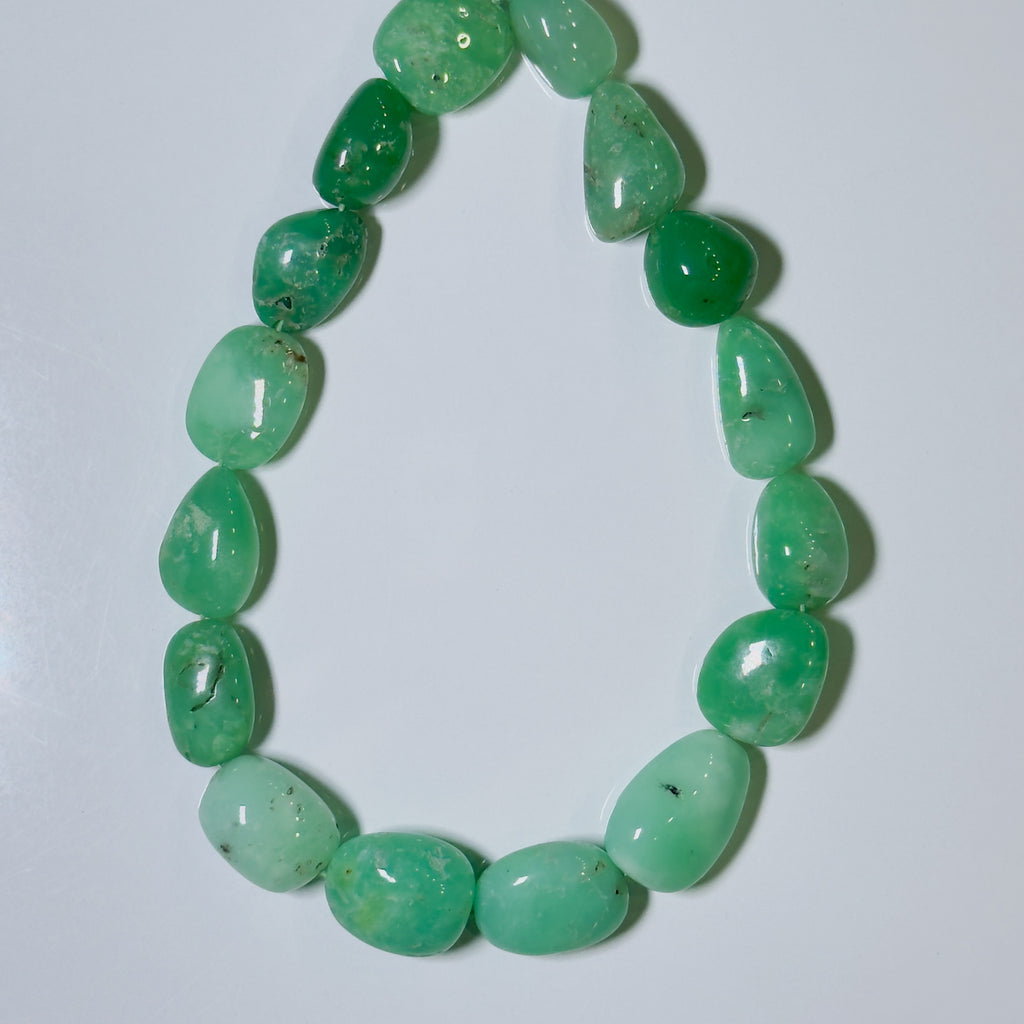 A beaded necklace made of polished, tumbled green gemstone beads with natural inclusions, arranged in an oval shape on a plain light gray background.