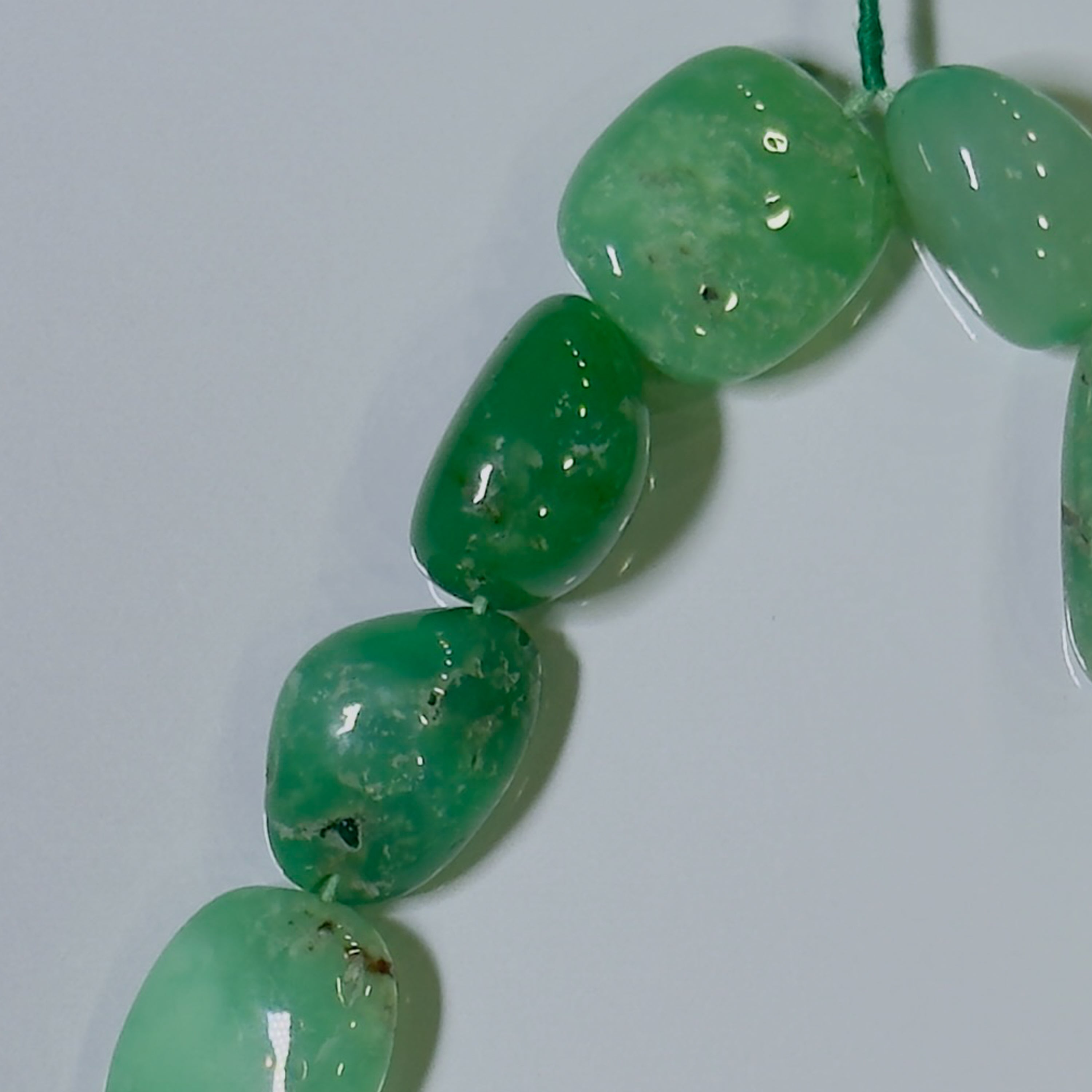 A close-up of glossy green stone beads strung on a cord against a plain light background.
