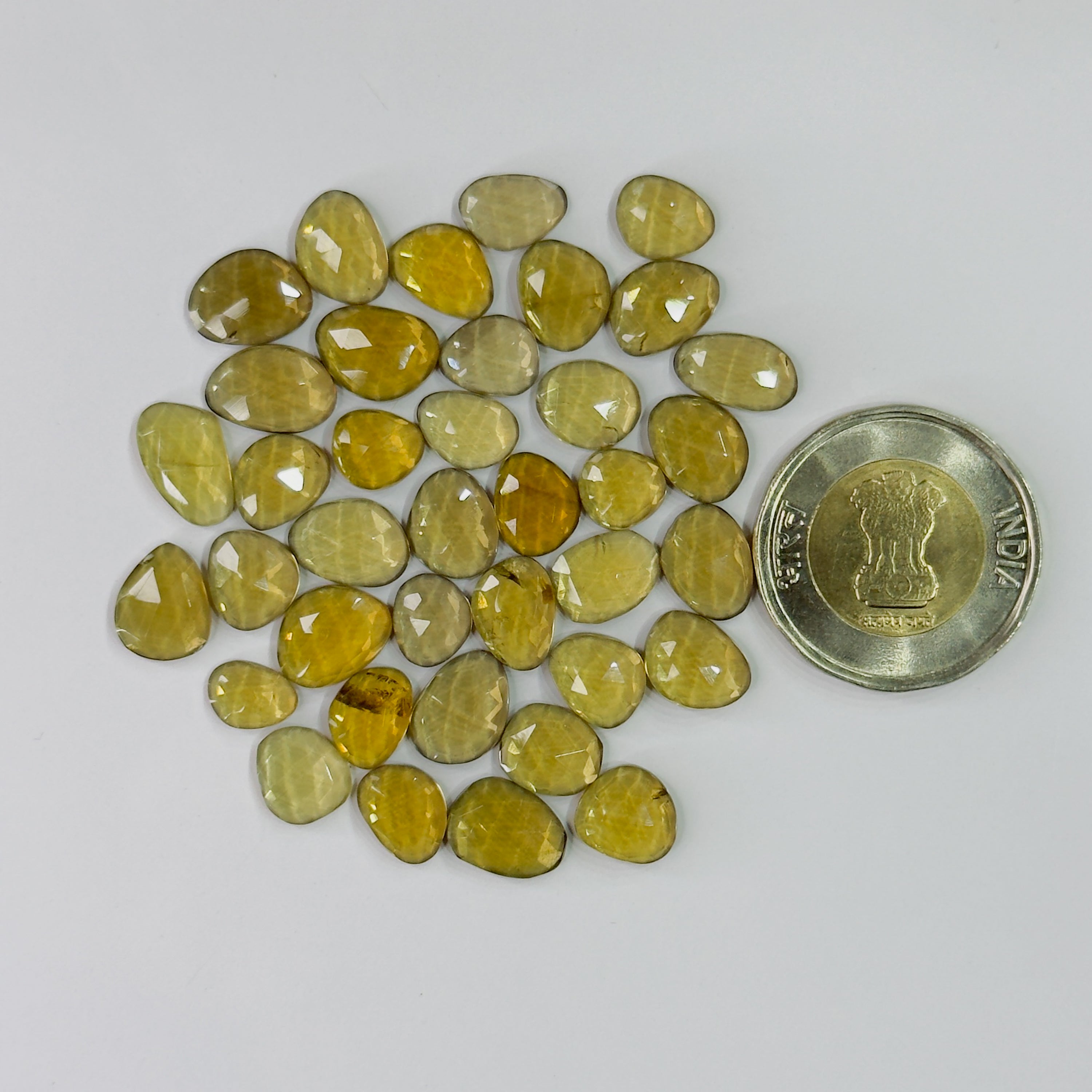 Yellow gemstones with a coin for scale on a white background