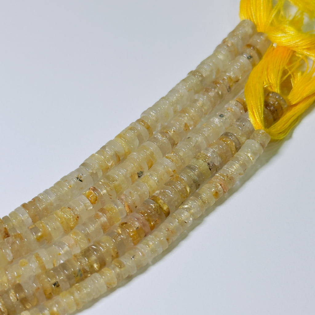 Close-up of a string of small, round, beige beads with a yellow thread on a white background.