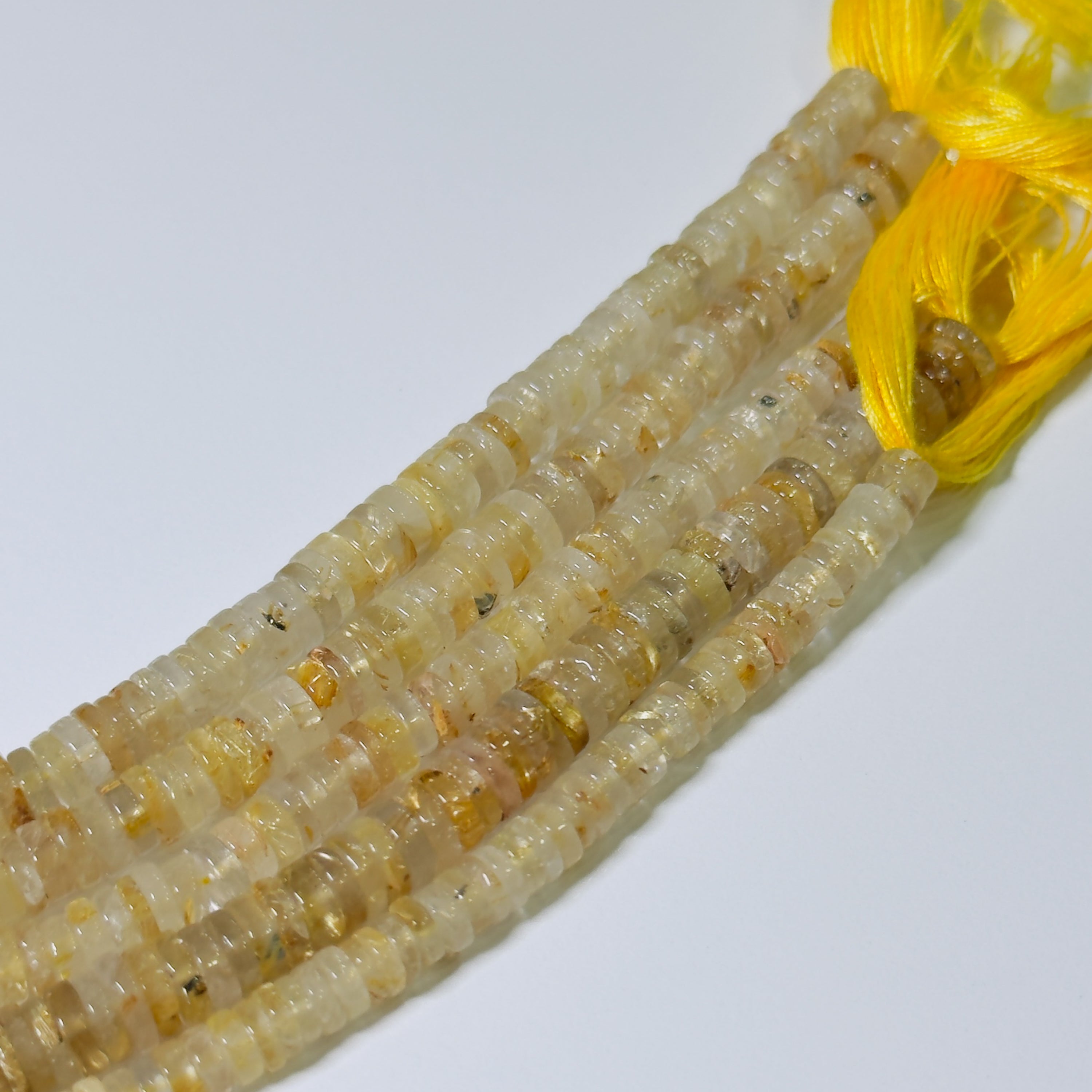 Close-up of a string of small, round, beige beads with a yellow thread on a white background.