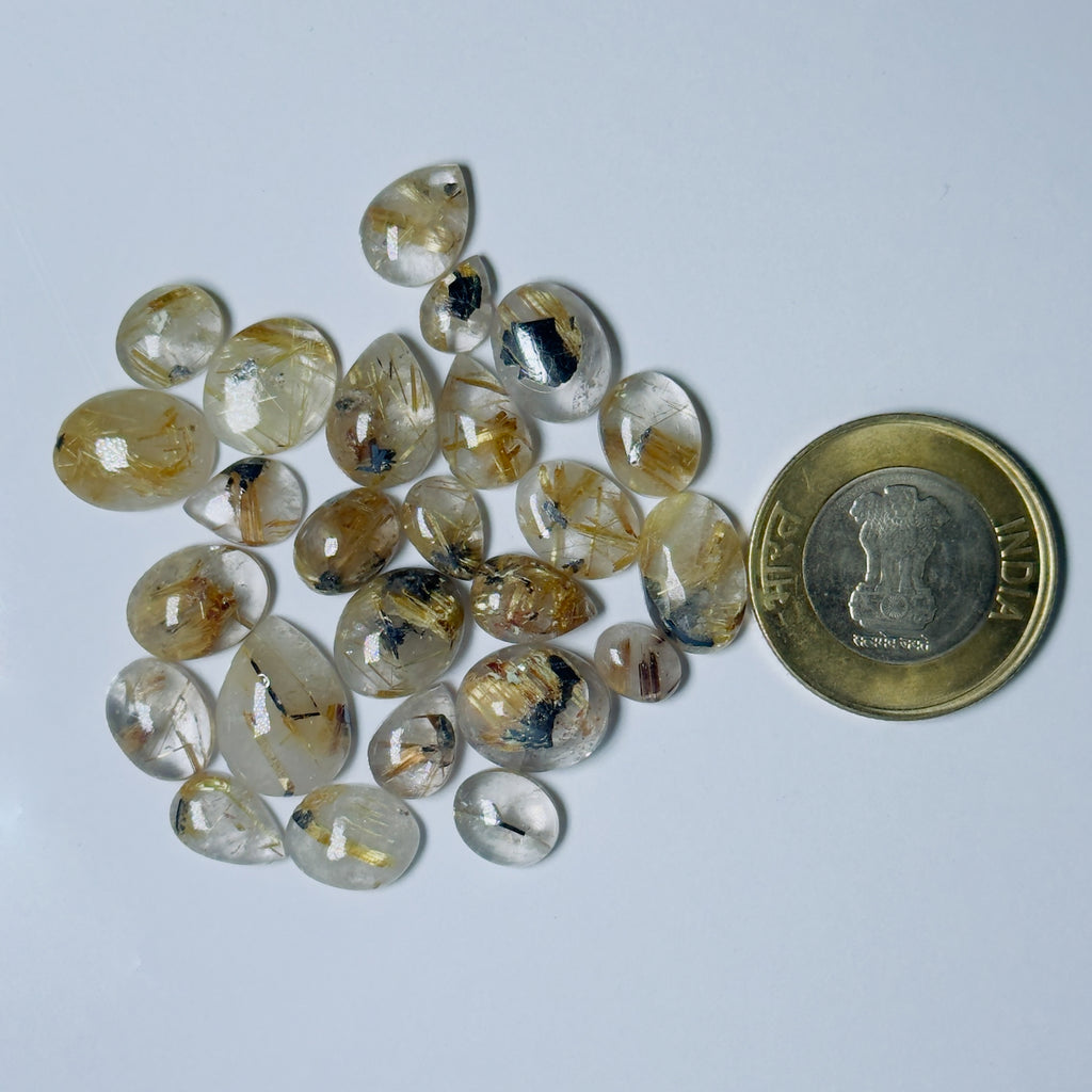 Teardrop-shaped gemstones with a coin for scale on a light gray background
