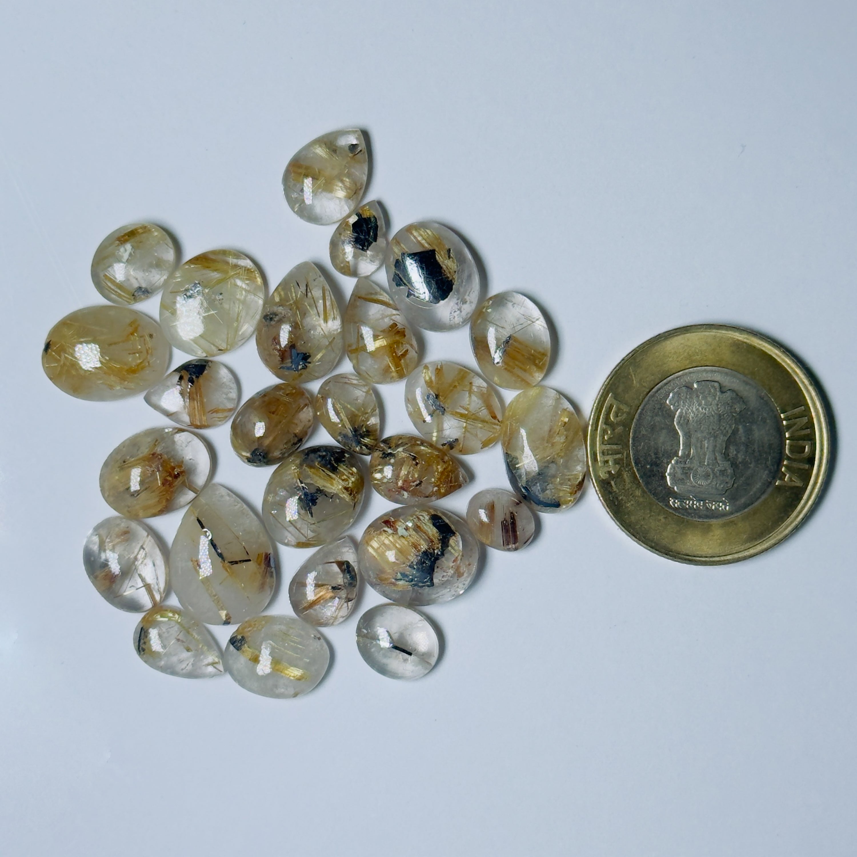 Teardrop-shaped gemstones with a coin for scale on a light gray background