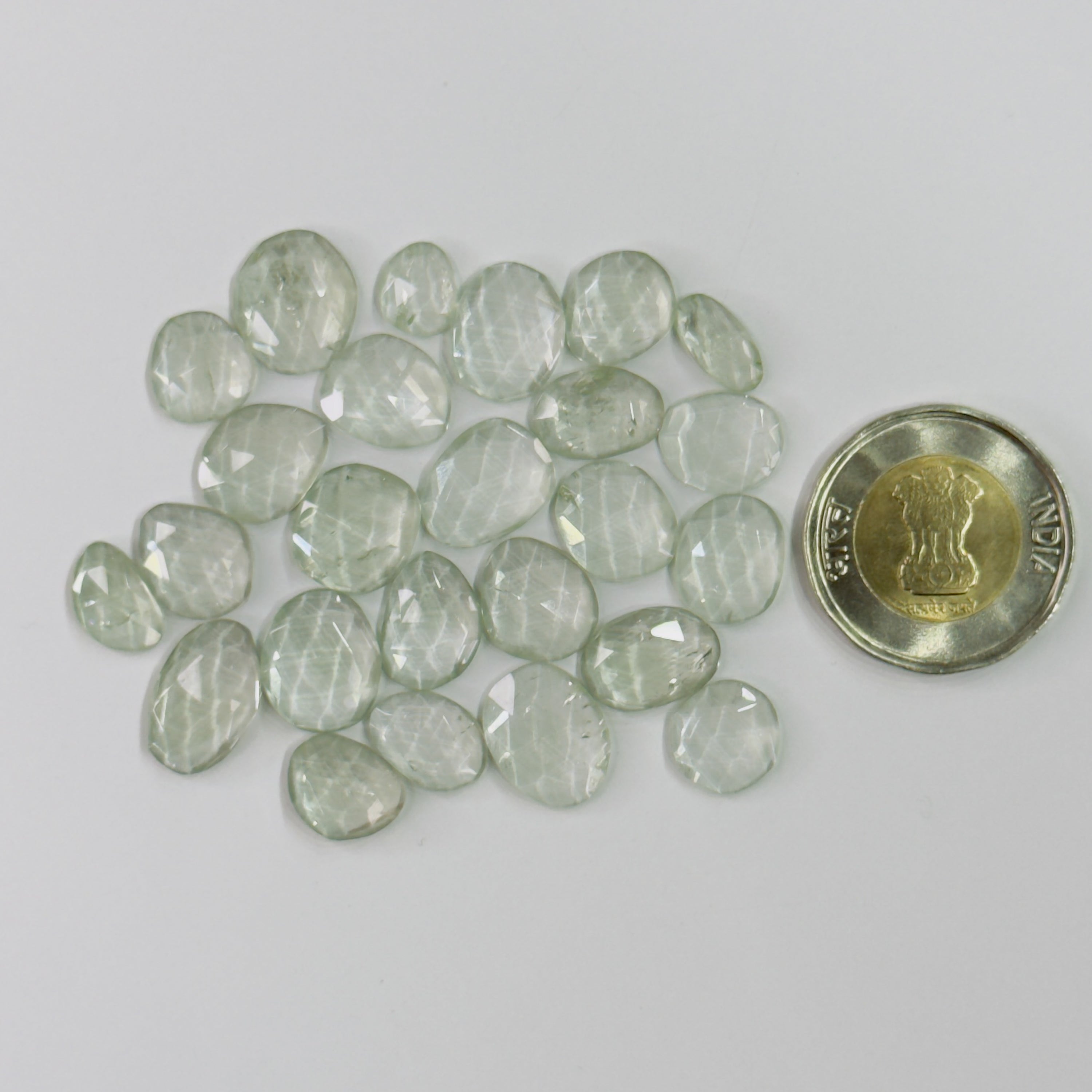 Green gemstones next to a coin on a white background