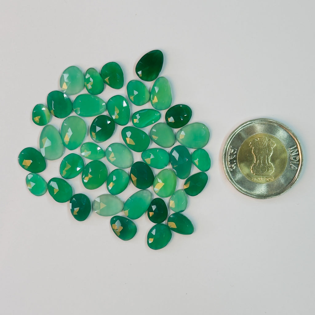 Green gemstones with a coin for scale on a white background