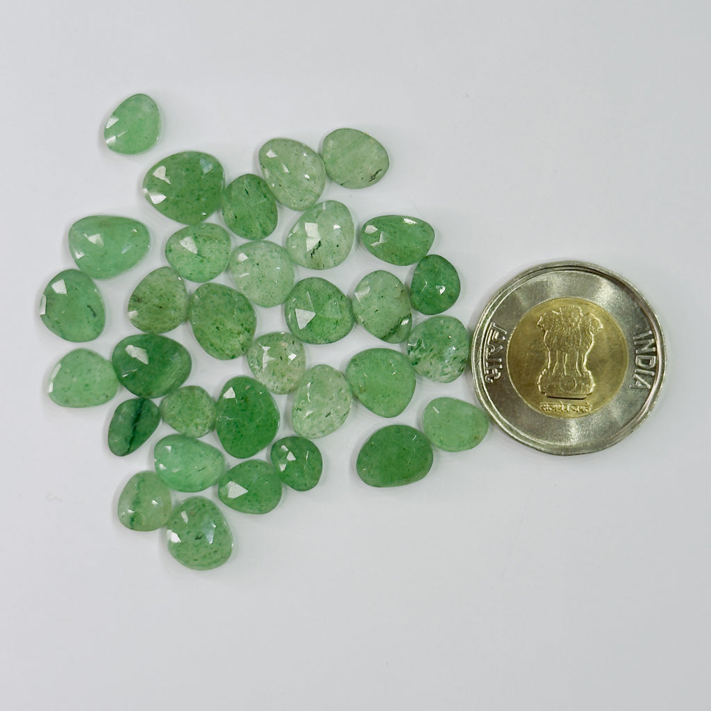 Green gemstones with a coin for scale on a white background