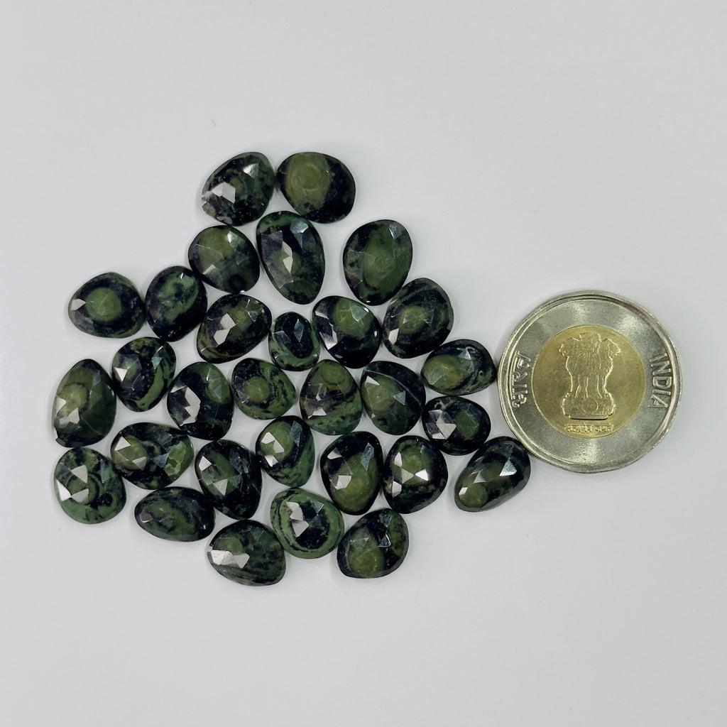 Teardrop-shaped green gemstones with a coin for scale on a white background
