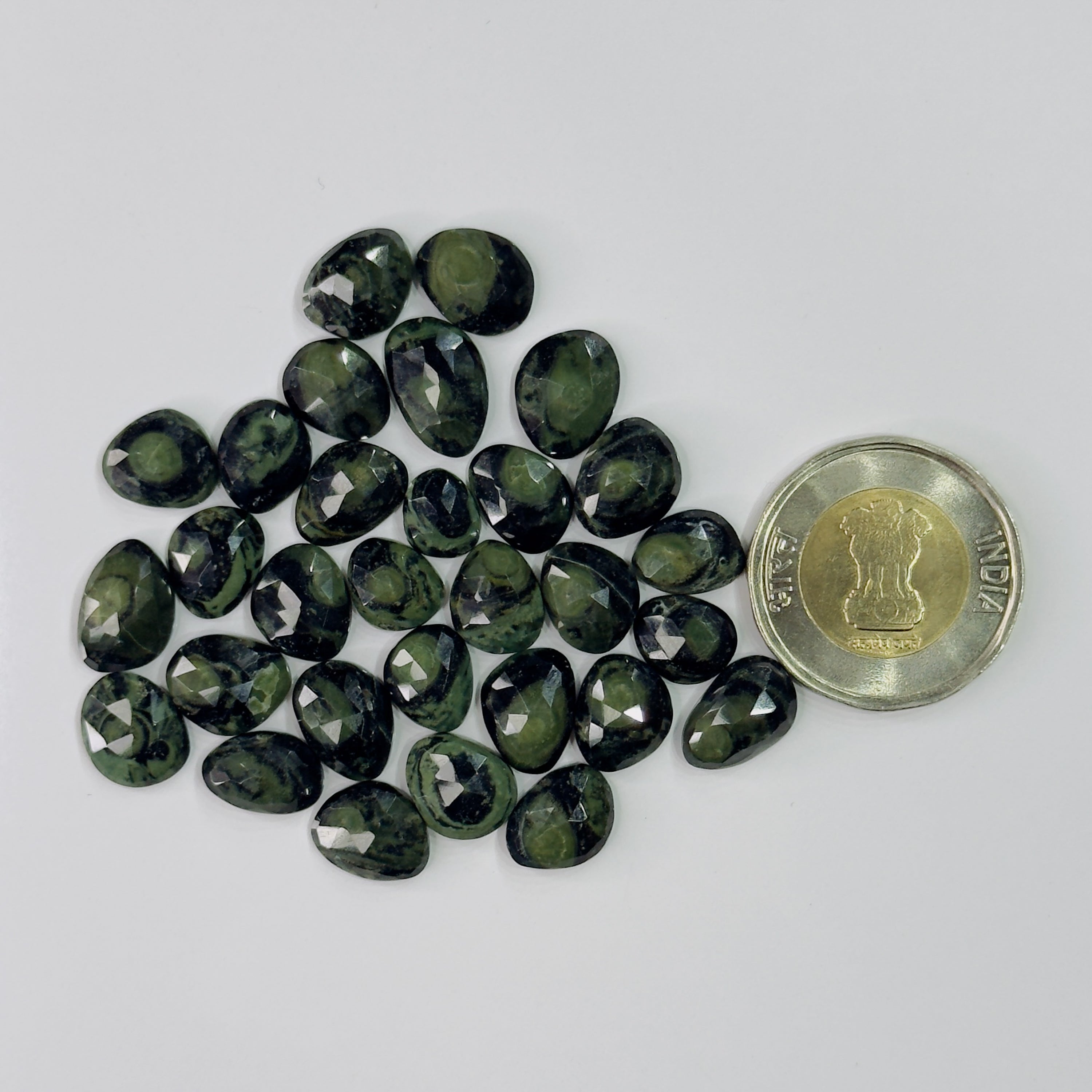Teardrop-shaped green gemstones with a coin for scale on a white background