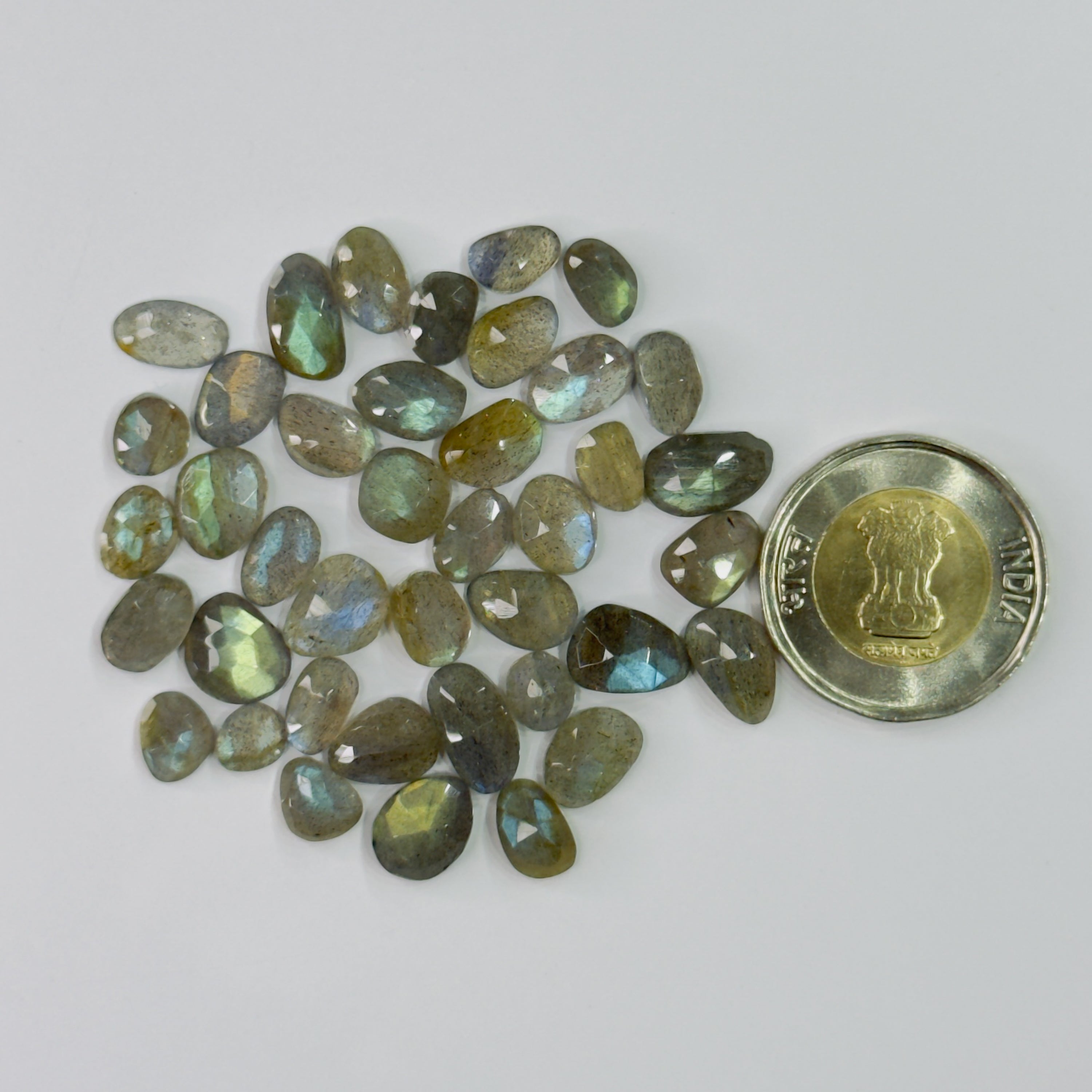 Collection of pear-shaped gemstones with a coin for scale on a white background