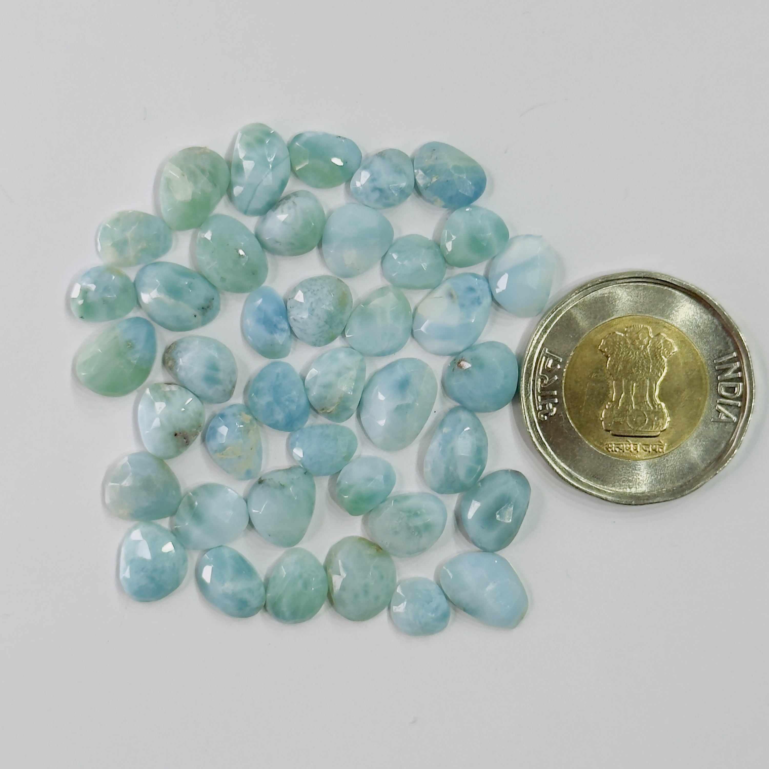 Turquoise-colored stones with a coin for scale on a white background