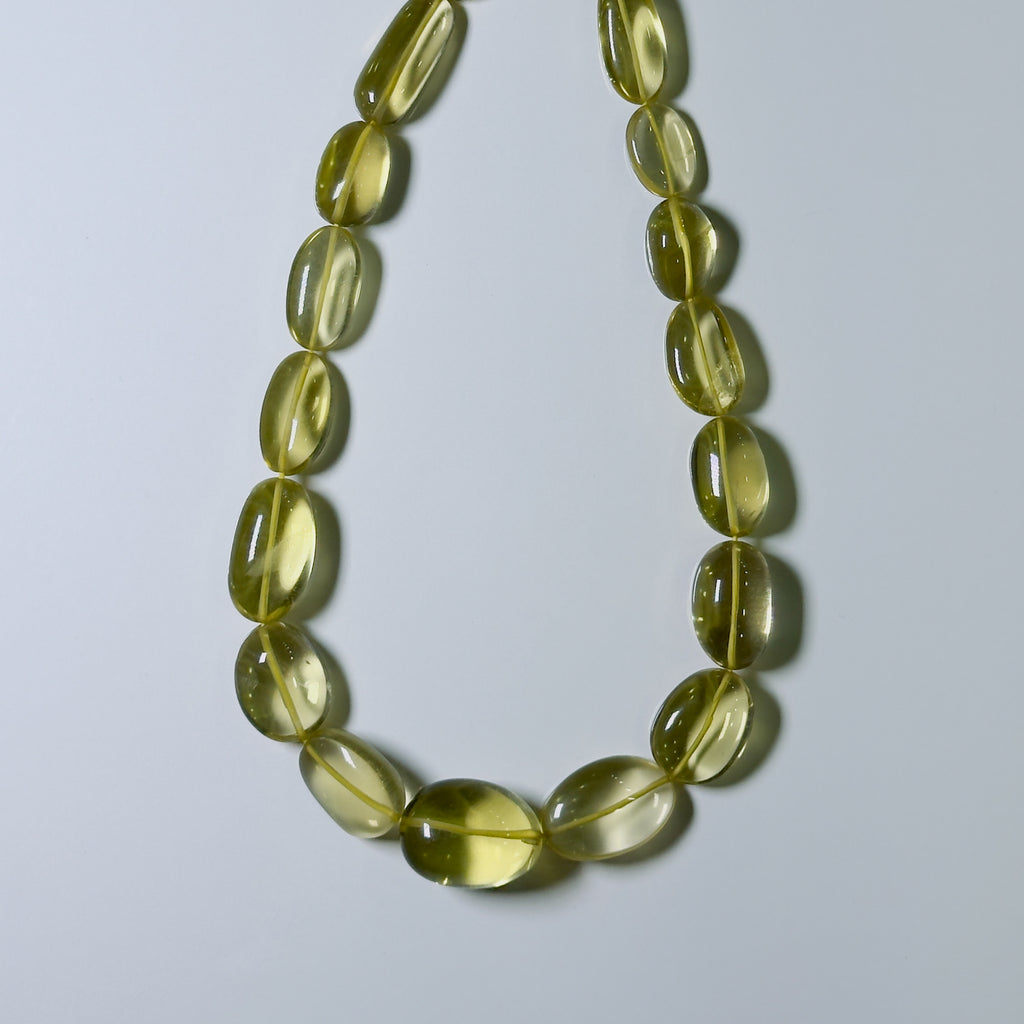 A translucent olive-green glass bead necklace arranged in a circle on a light gray background.