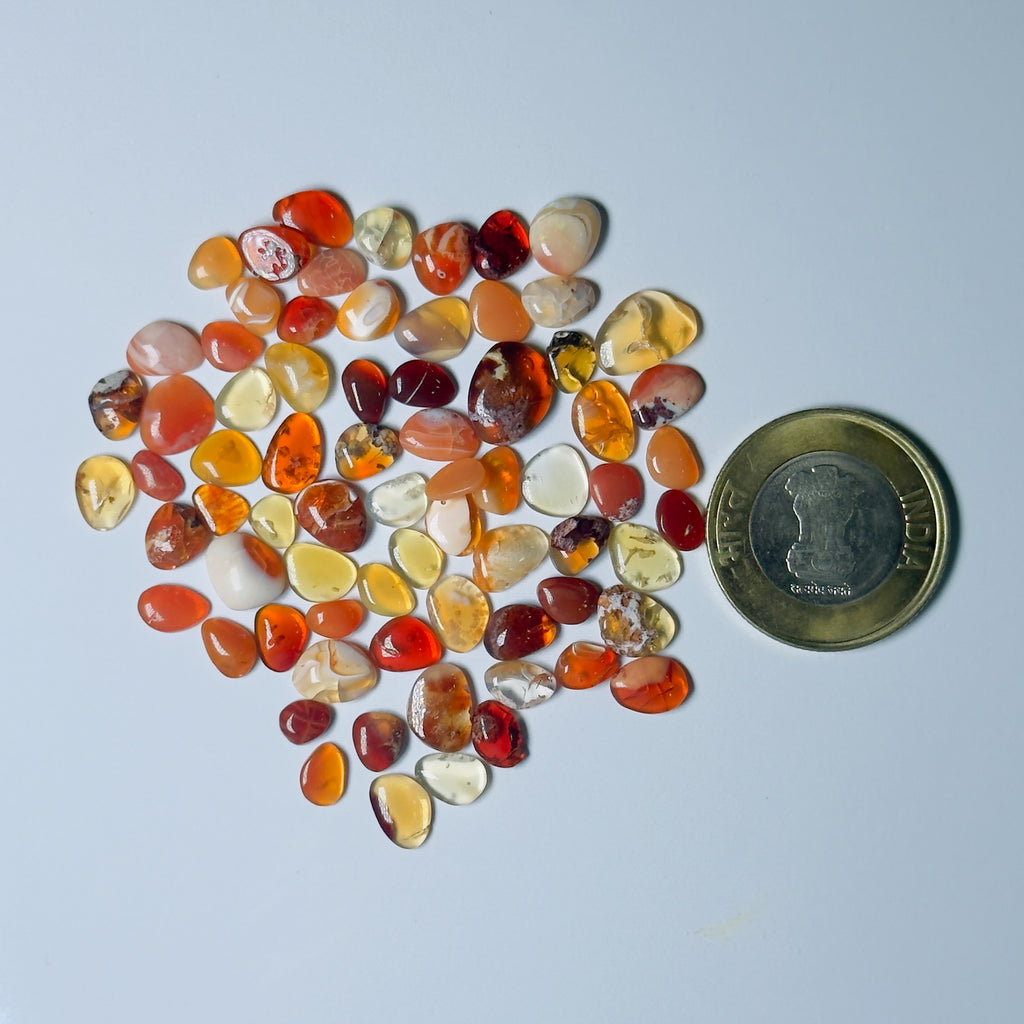 Assorted colored stones arranged in a heart shape with a coin for scale on a white background