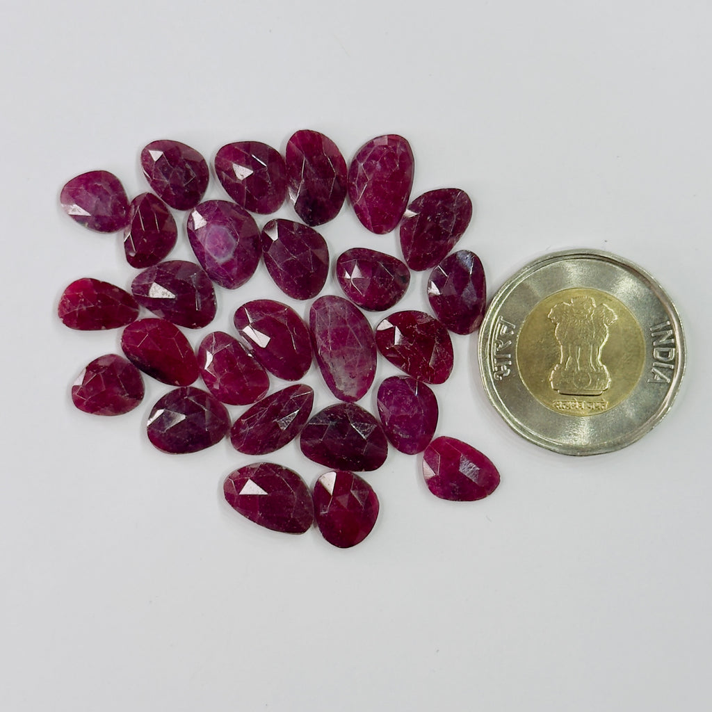 Collection of red gemstones next to a coin on a white background