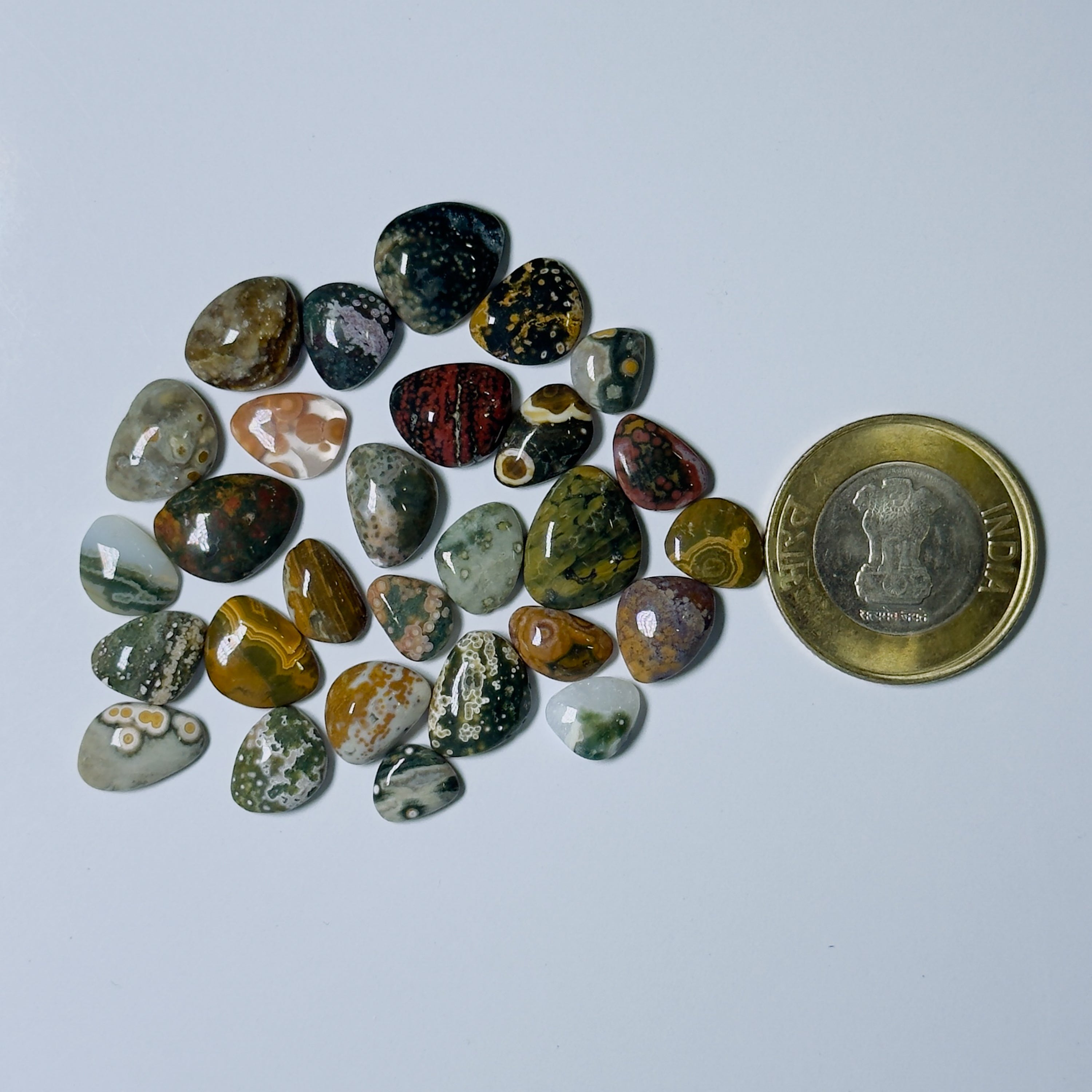 Collection of multicolored stones on a white background with a coin for scale.
